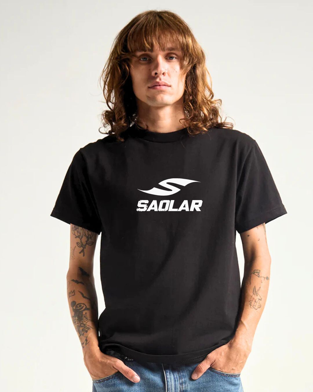 Male model wearing black SAOLAR t-shirt with bold white sport sunglasses logo, casual style, visible tattoos, hands in pockets.
