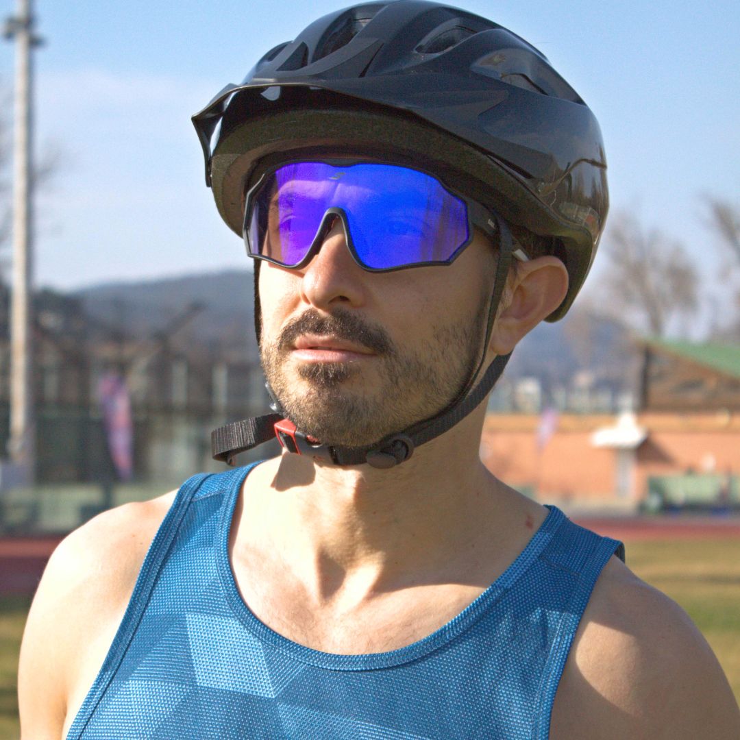 Man wearing SAOLAR Aquavex photochromic sports sunglasses with striking blue-purple mirrored lenses and black frame, standing outdoors in athletic gear.