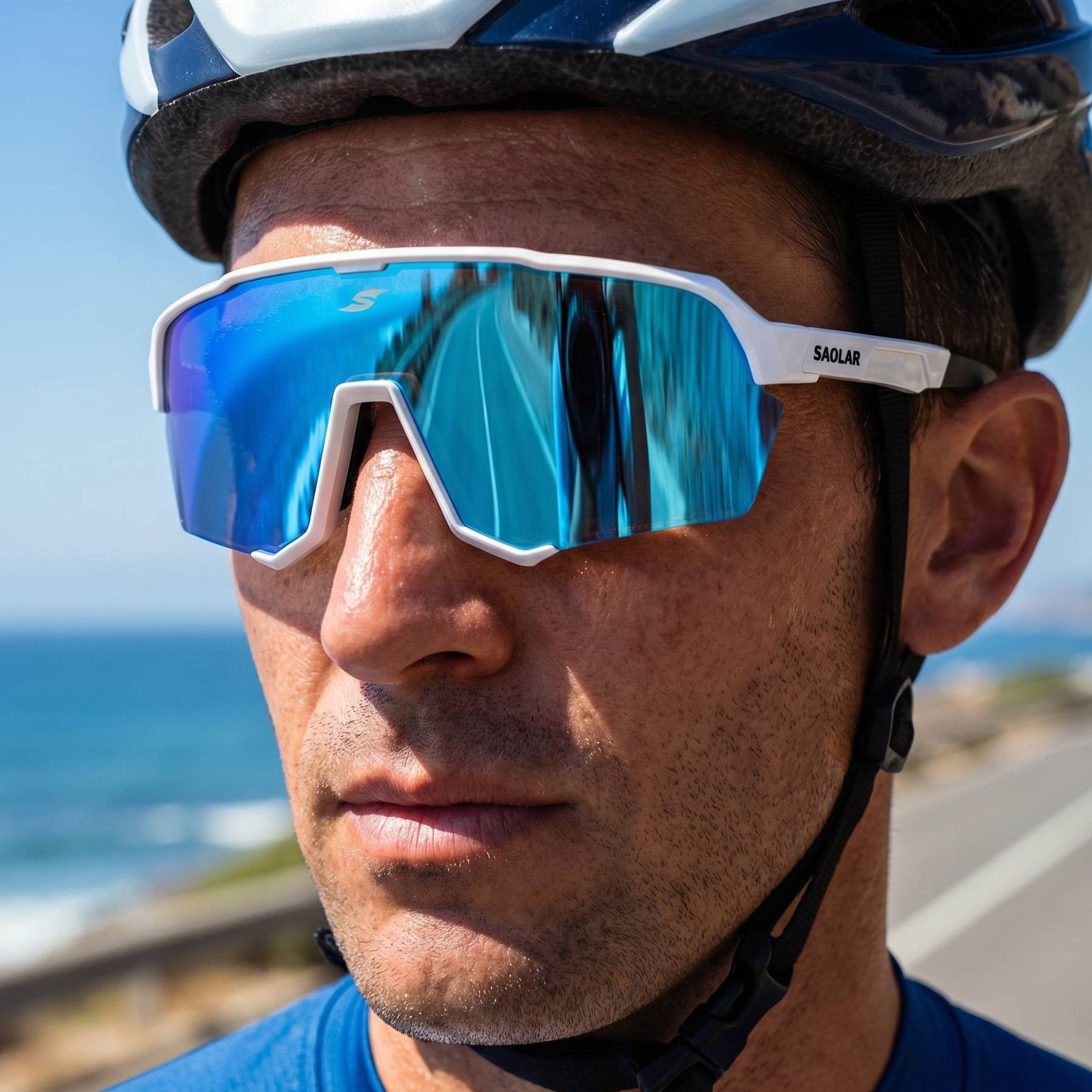 Close-up of cyclist wearing SAOLAR EmberLine Ice photochromic sport sunglasses with full revo blue lenses. Lightweight white wraparound frame delivers panoramic vision, UV400 protection, and anti glare clarity. Ideal for cycling and outdoor performance, offering comfort, stability, and sharp vision in bright coastal conditions and changing light environments.