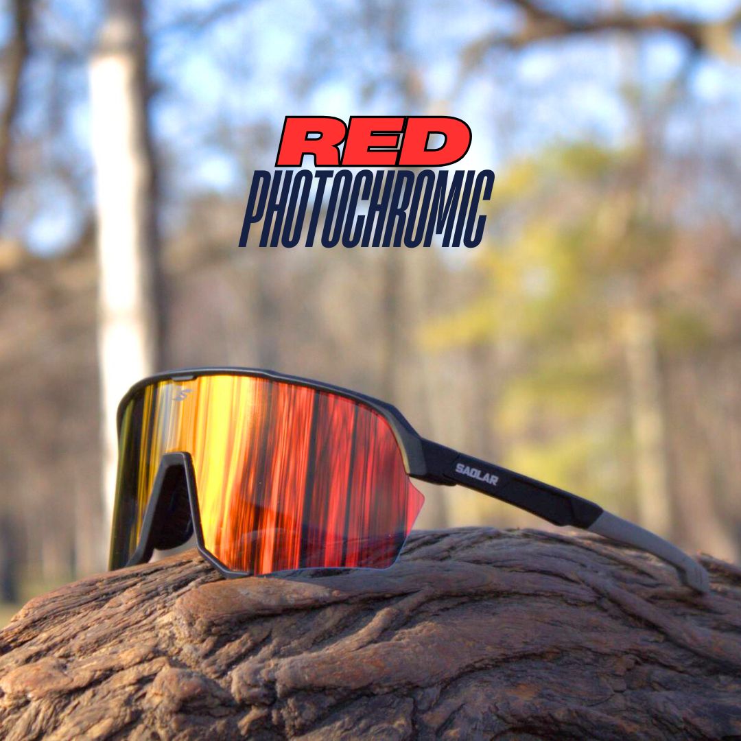 SAOLAR Emberline red photochromic sunglasses with a black frame and wraparound lens, resting on textured wood in an outdoor setting.