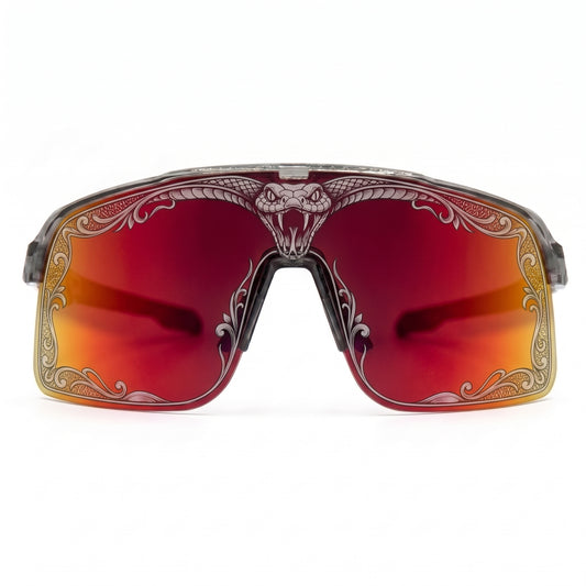 Front view of SAOLAR Flareforce Venom cycling sunglasses featuring a large red-to-orange mirrored shield lens, transparent frame and detailed snake and ornamental laser artwork around the lens edge. These distinctive performance sunglasses combine panoramic vision, wraparound protection and bold design for cycling, running and other outdoor sports.
