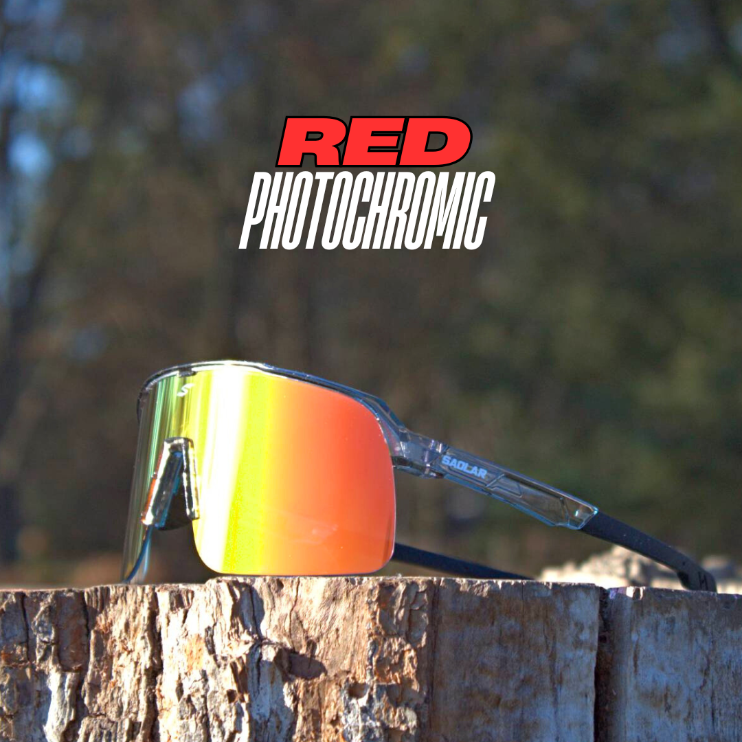 SAOLAR red photochromic sunglasses with a wraparound shield lens, clear frame, and black temples, placed on a wooden surface outdoors.