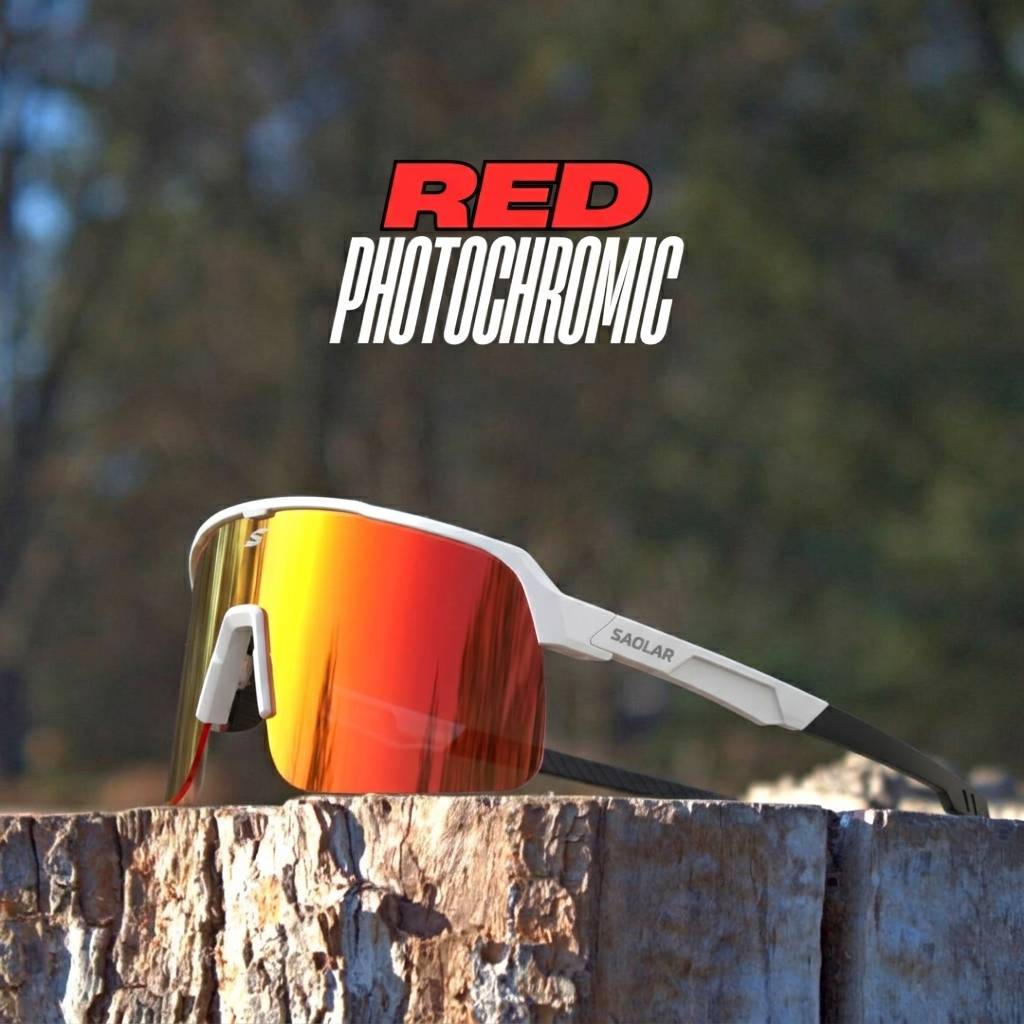 SAOLAR Flareforce Kingsnake red photochromic sunglasses with a wraparound shield lens, clear frame, and black temples, placed on a wooden surface outdoors.