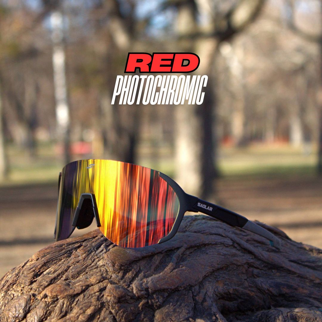 SAOLAR Hyperion red photochromic sunglasses with a black frame and wraparound lens, placed on textured wood in a park setting.