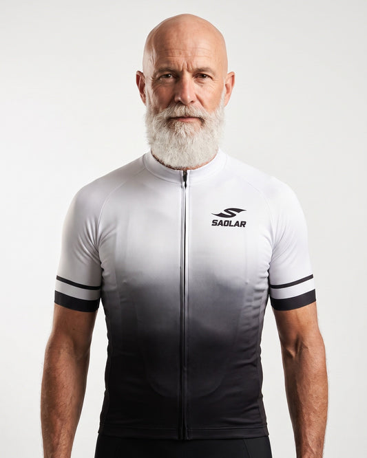 Front studio view of a mature male cyclist wearing the SAOLAR Gradient cycling jersey. The fitted short-sleeve jersey transitions from white at the shoulders to black at the waist, with striped sleeve bands, a full-length zipper, and the black SAOLAR logo displayed on the chest against a clean white background.