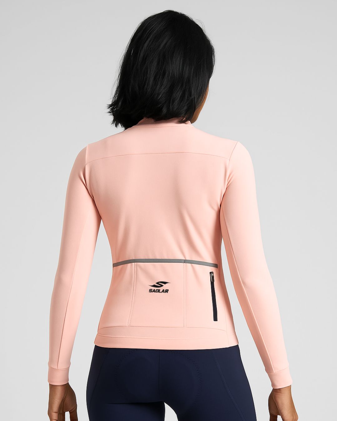 Woman wearing the SAOLAR S2 Aurora long sleeve cycling jersey in soft pink, shown from the back with reflective details.