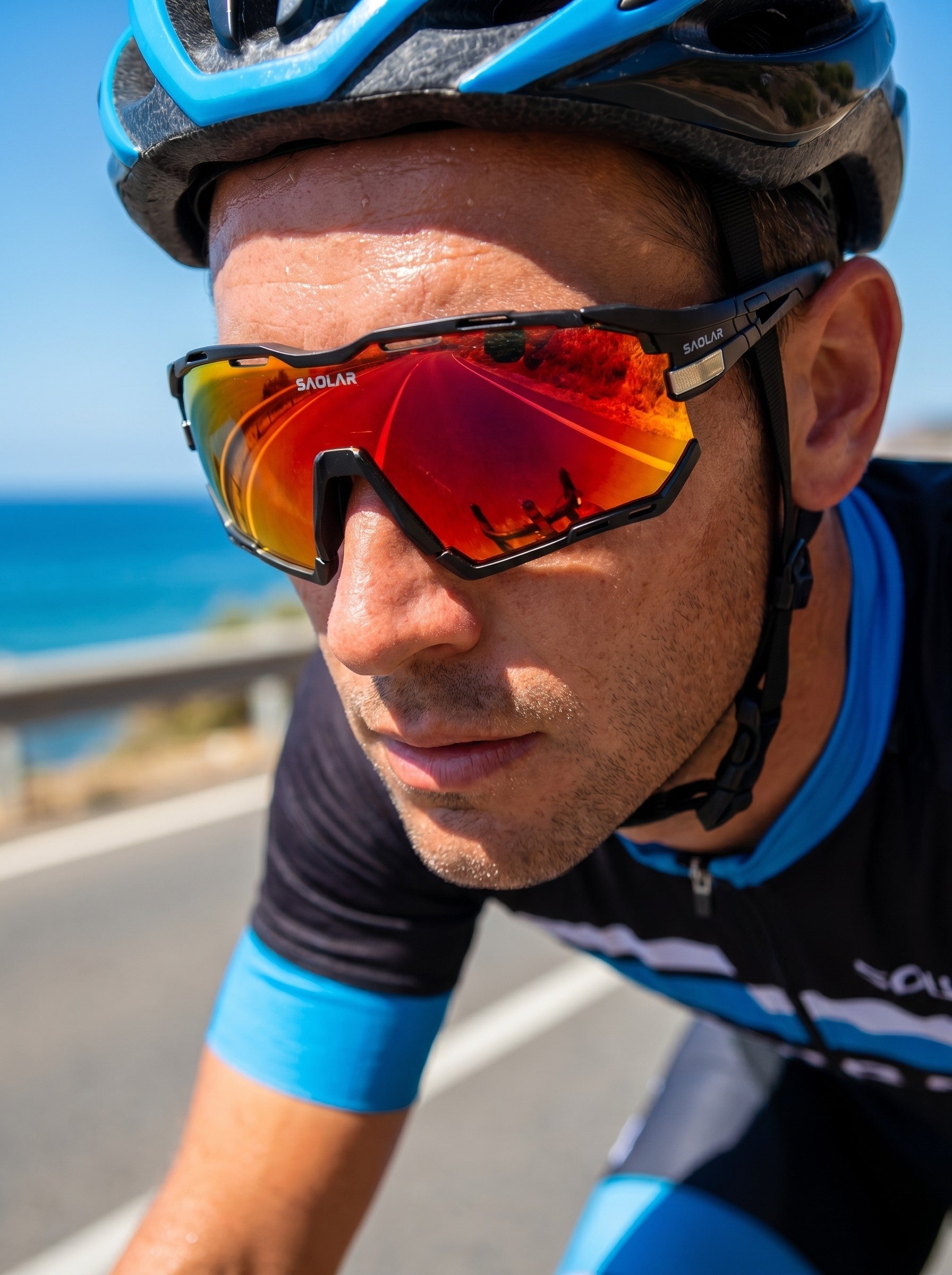 SAOLAR Rapture photochromic cycling sunglasses with full revo mirrored lens, worn by cyclist riding on coastal road under bright sunlight. Lightweight wraparound frame offers wind protection, panoramic vision, and UV400 defense. Lenses automatically adapt to light conditions, enhancing contrast and clarity for high-performance road cycling and outdoor sports activities.