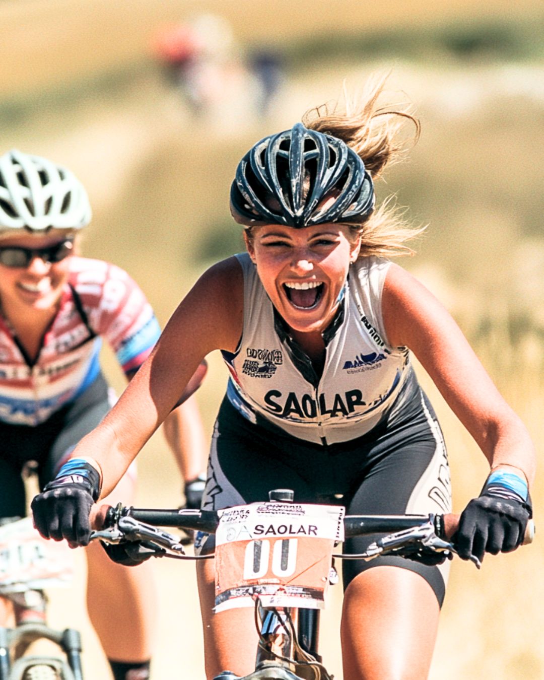 Two excited cyclists racing, wearing SAOLAR-branded gear and helmets, showcasing energy, adventure, and high-performance spirit in outdoor biking.